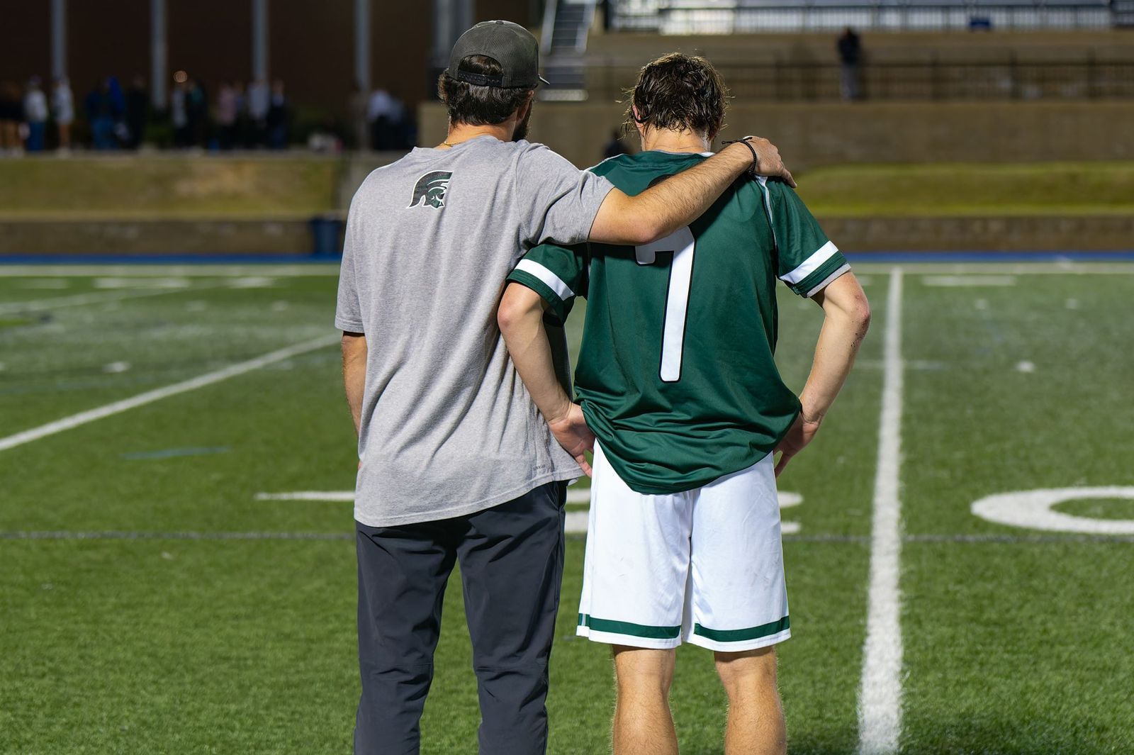 A mentor standing with his arm around a young athlete on the sideline